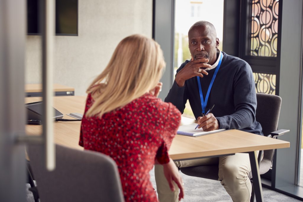Person visiting an Advisor in a office around a table while they are sat down. 